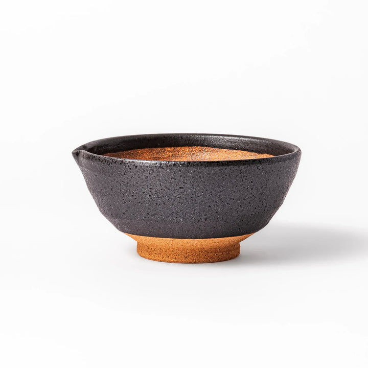 Black ceramic suribachi mortar bowl with brown textured grooves and spout for grinding sesame seeds.