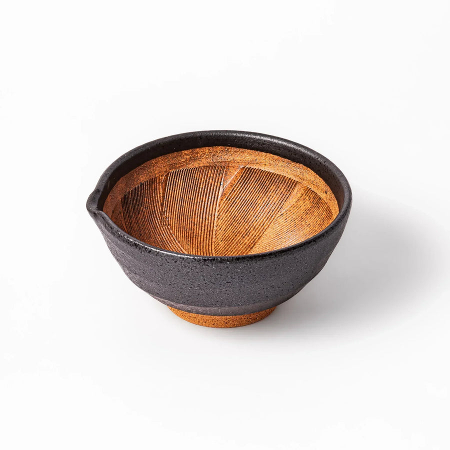 Black ceramic suribachi mortar bowl with brown textured grooves and spout for grinding sesame seeds.