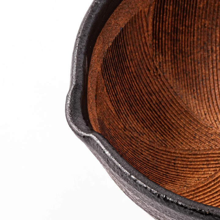 Black ceramic suribachi mortar bowl with brown textured grooves and spout for grinding sesame seeds.