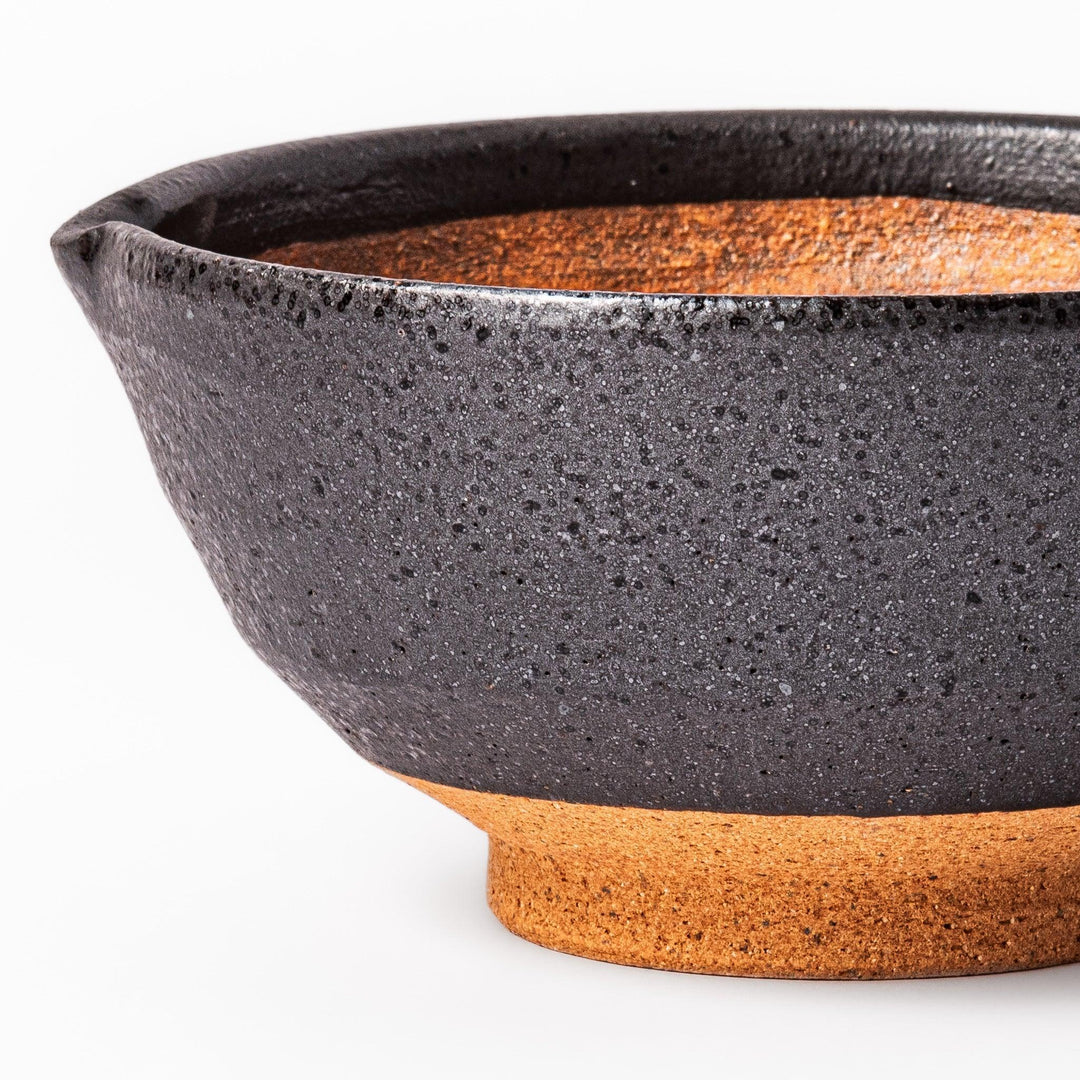 Black ceramic suribachi mortar bowl with brown textured grooves and spout for grinding sesame seeds.