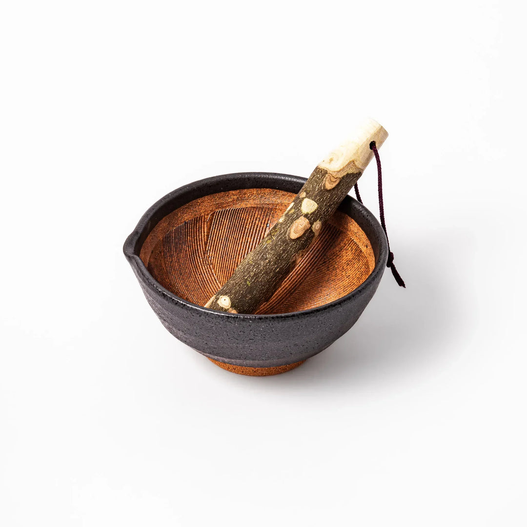 Black Japanese ceramic suribachi mortar with brown grooved interior and wood pestle for sesame grinding.