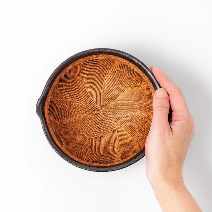 Black ceramic suribachi mortar bowl with brown textured grooves and spout for grinding sesame seeds.