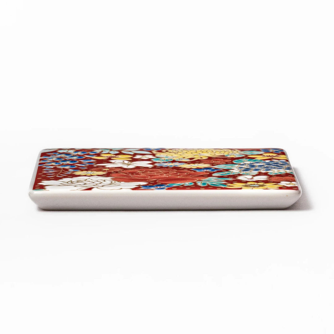 Square Japanese ceramic coaster with vivid red base featuring peony, chrysanthemum, and floral motifs in multicolor design.