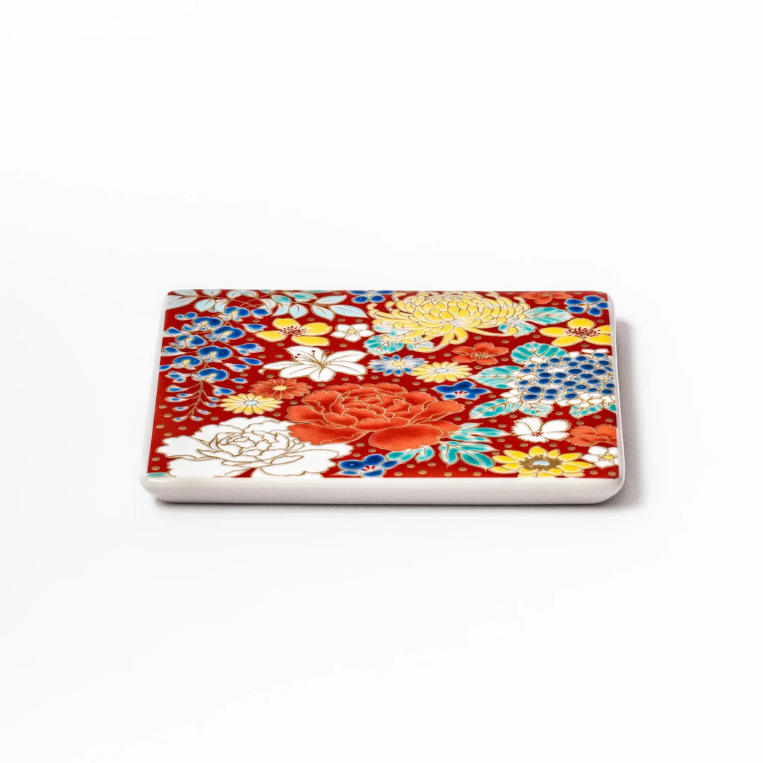 Square Japanese ceramic coaster with vivid red base featuring peony, chrysanthemum, and floral motifs in multicolor design.