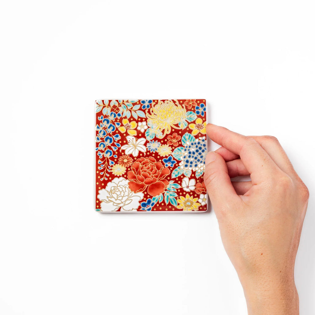 Square Japanese ceramic coaster with vivid red base featuring peony, chrysanthemum, and floral motifs in multicolor design.