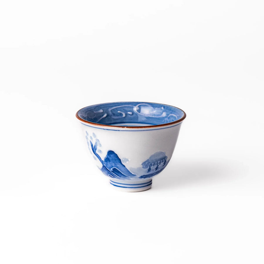 Porcelain sake cup with hand-painted blue mountain and cloud motifs, featuring a red rim and classic Japanese design.