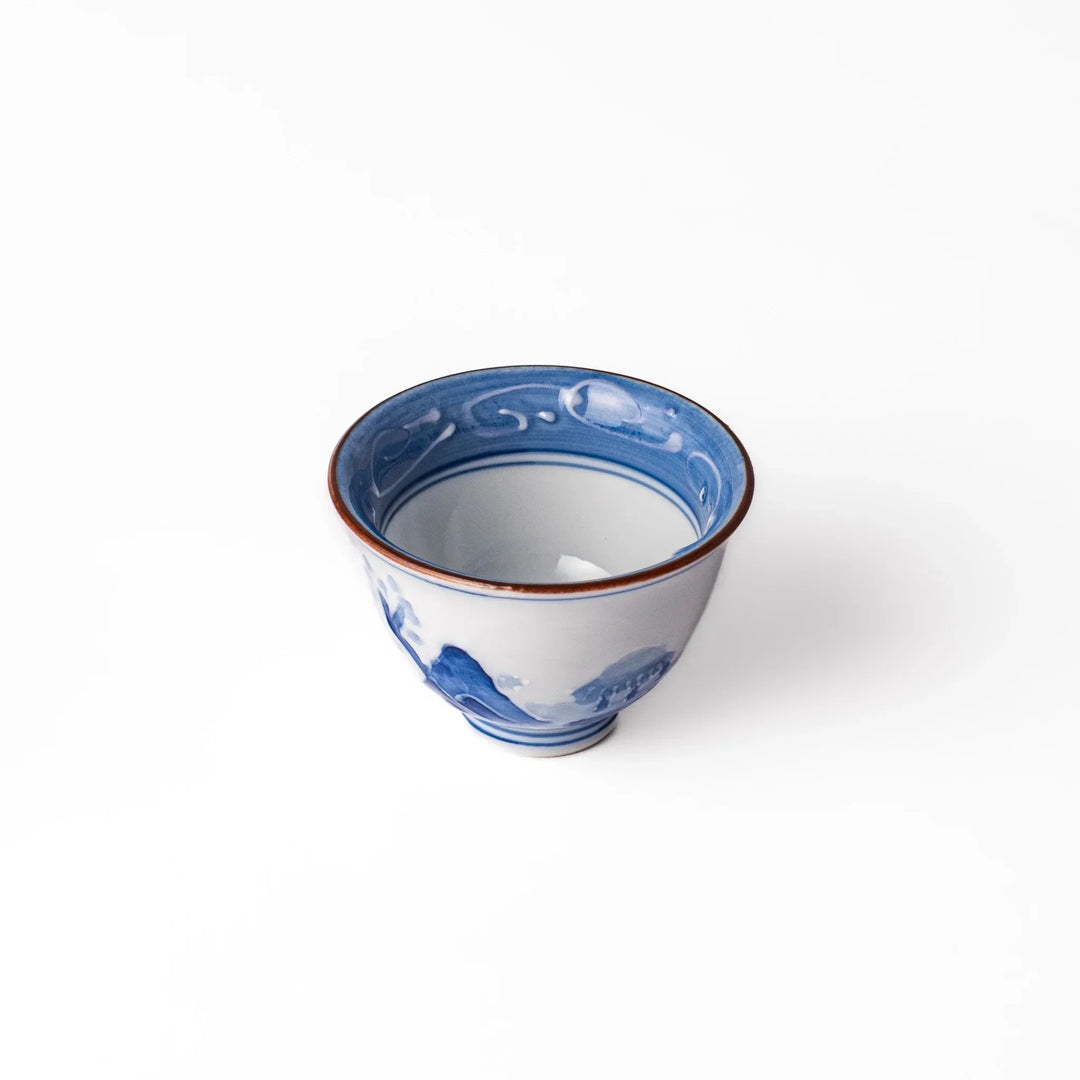 Porcelain sake cup with hand-painted blue mountain and cloud motifs, featuring a red rim and classic Japanese design.