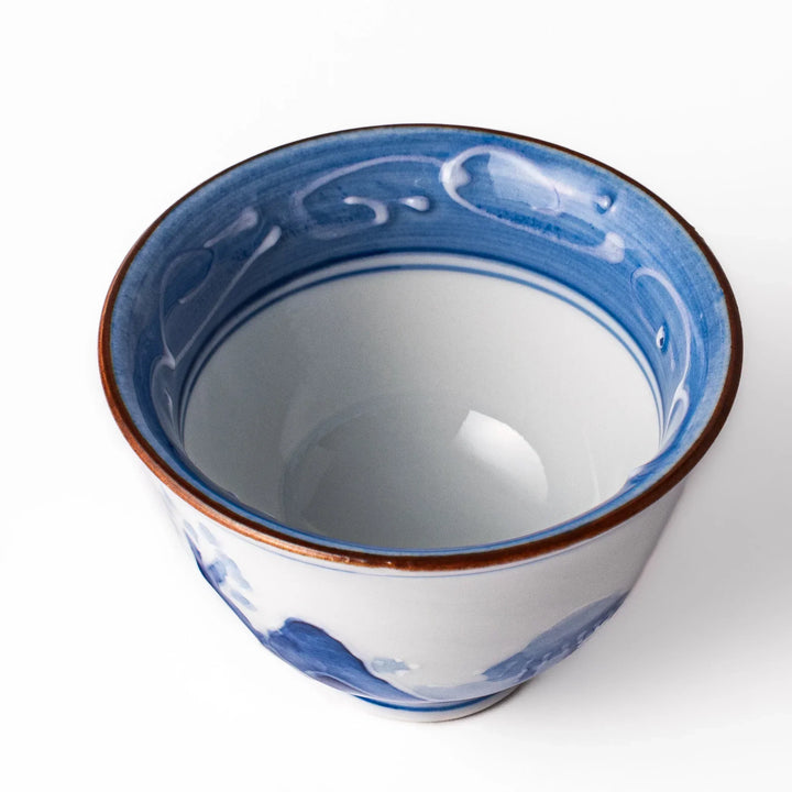 Porcelain sake cup with hand-painted blue mountain and cloud motifs, featuring a red rim and classic Japanese design.