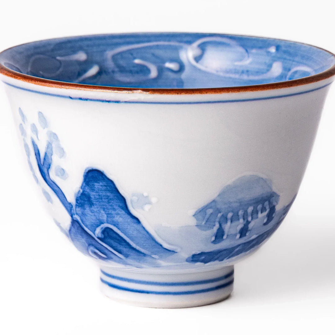 Porcelain sake cup with hand-painted blue mountain and cloud motifs, featuring a red rim and classic Japanese design.
