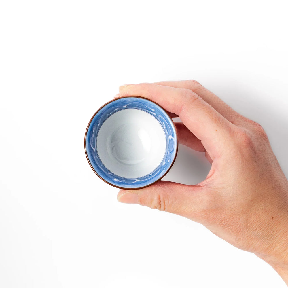 Porcelain sake cup with hand-painted blue mountain and cloud motifs, featuring a red rim and classic Japanese design.