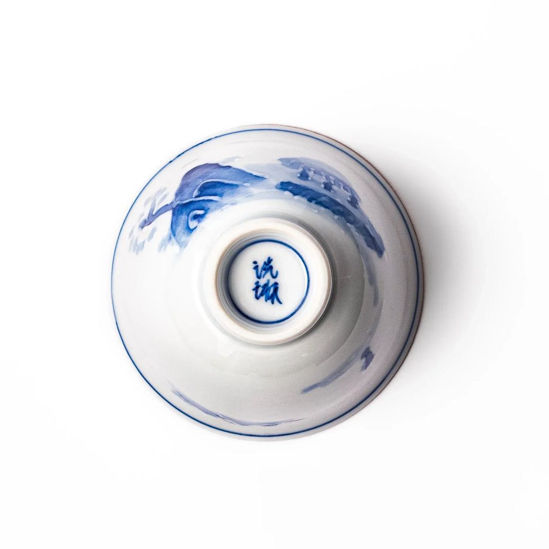 Porcelain sake cup with hand-painted blue mountain and cloud motifs, featuring a red rim and classic Japanese design.