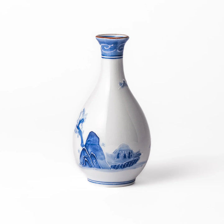 Porcelain sake flask with hand painted blue mountain and village scene red rim and elegant traditional shape.
