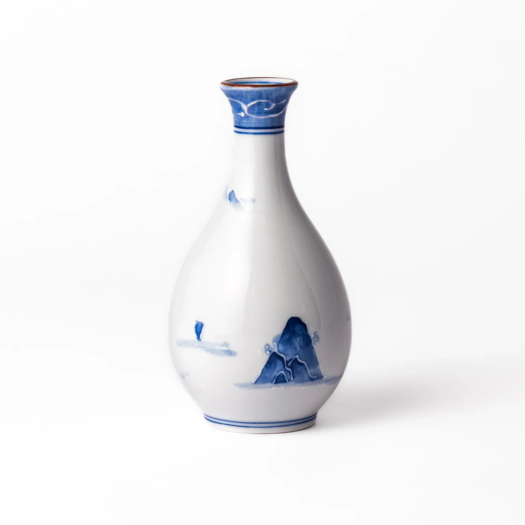 Porcelain sake flask with hand painted blue mountain and village scene red rim and elegant traditional shape.