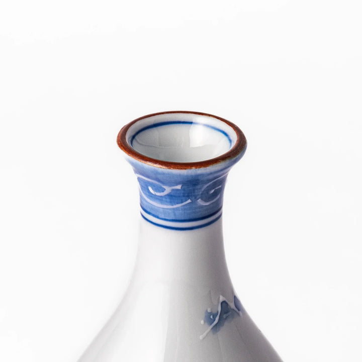 Porcelain sake flask with hand painted blue mountain and village scene red rim and elegant traditional shape.