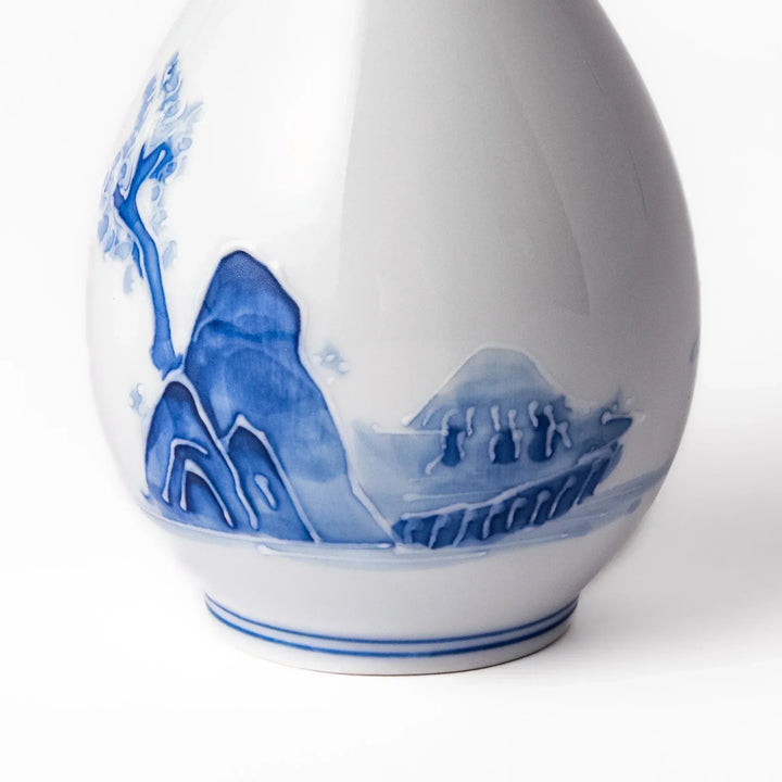 Porcelain sake flask with hand painted blue mountain and village scene red rim and elegant traditional shape.
