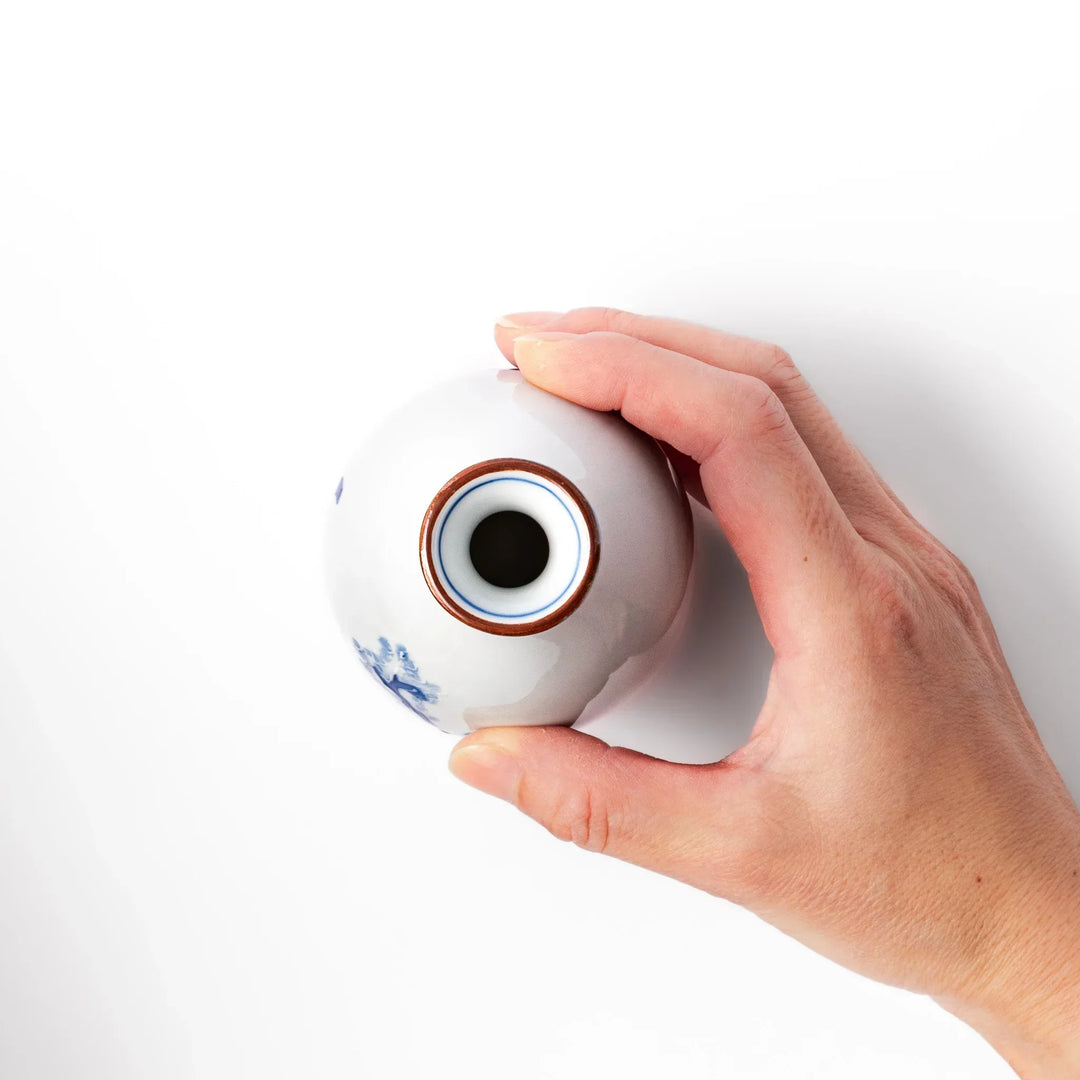 Porcelain sake flask with hand painted blue mountain and village scene red rim and elegant traditional shape.