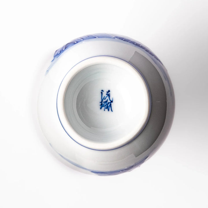 Porcelain sake flask with hand painted blue mountain and village scene red rim and elegant traditional shape.