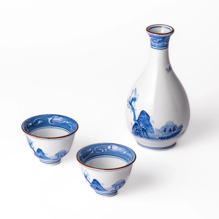 Three piece Japanese porcelain sake set with white flask and cups featuring blue wave and red brown rims.