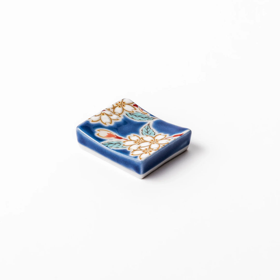Rectangular blue Japanese ceramic chopstick rest with white sakura blossoms and green leaves for dining.