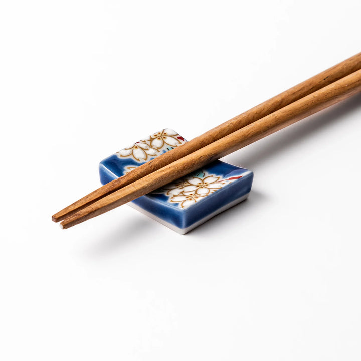 Rectangular blue Japanese ceramic chopstick rest with delicate white sakura blossoms and green leaves, ideal for traditional dining.