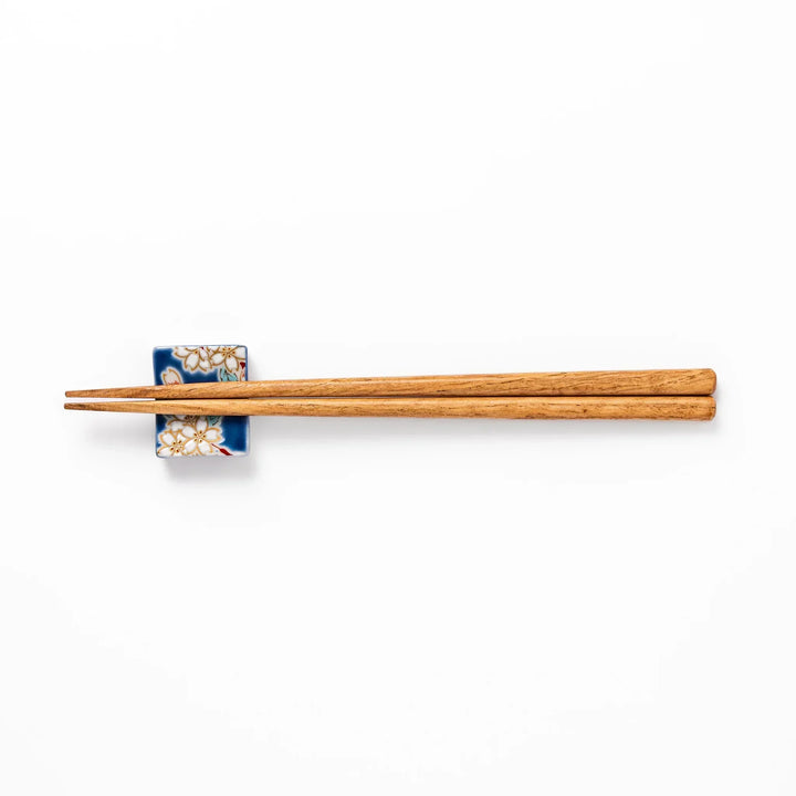 Rectangular blue Japanese ceramic chopstick rest with white sakura blossoms and green leaves for dining.