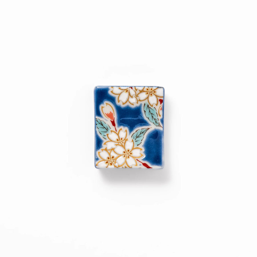 Rectangular blue Japanese ceramic chopstick rest with white sakura blossoms and green leaves for dining.