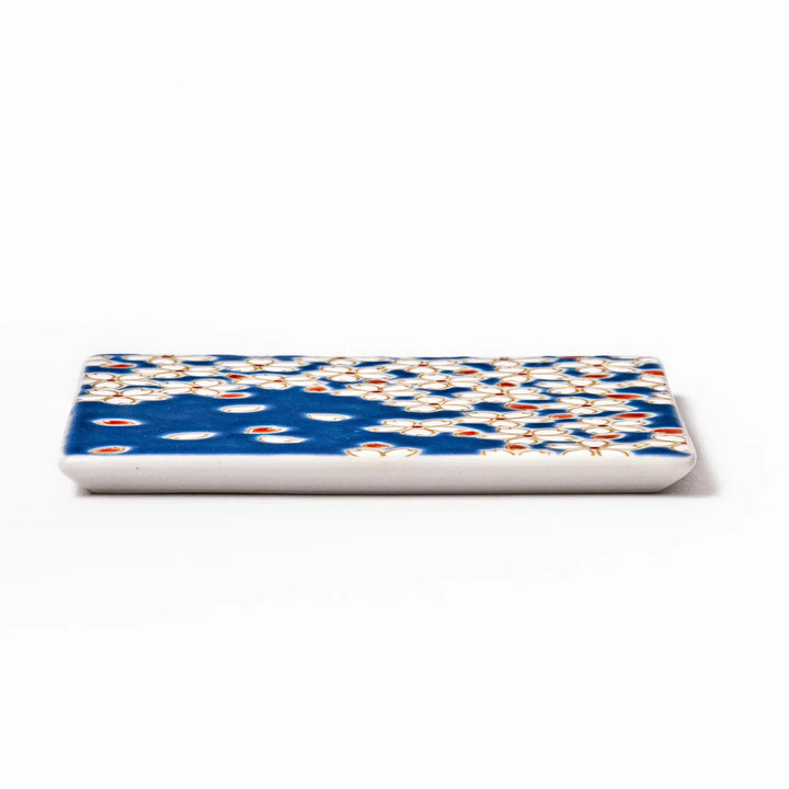 Square blue Japanese ceramic coaster with white sakura blossom and petal design for traditional dining.
