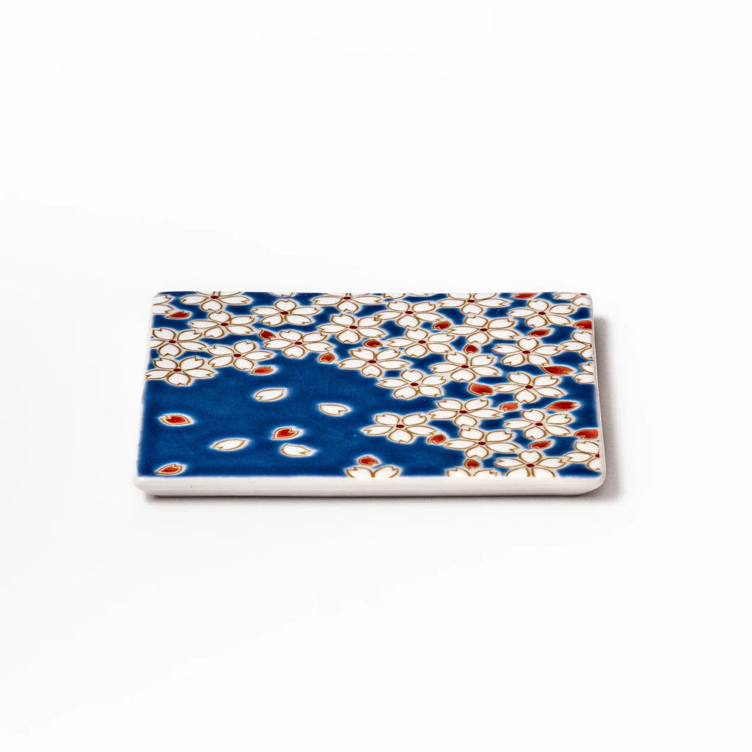 Square blue Japanese ceramic coaster with white sakura blossom and petal design for traditional dining.