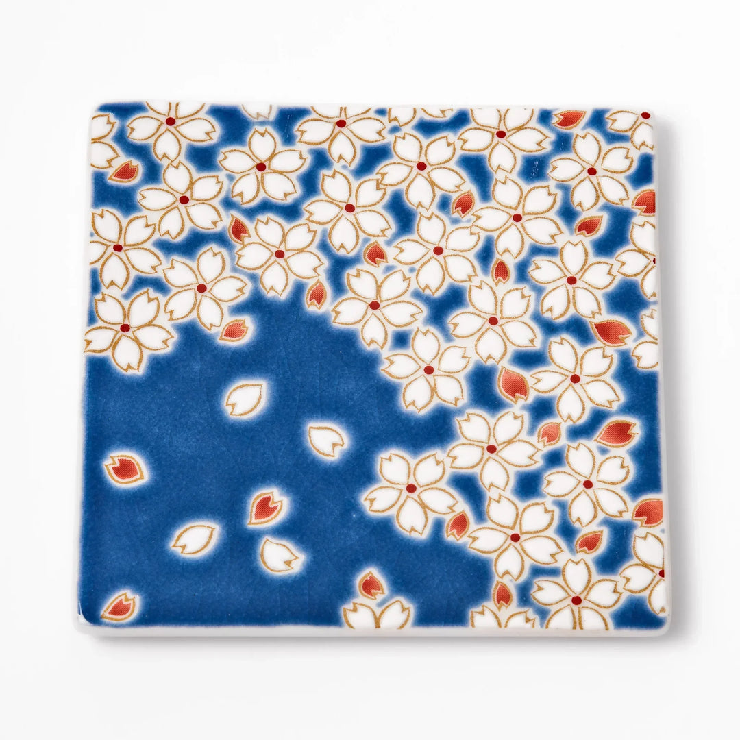 Square blue Japanese ceramic coaster with white sakura blossom and petal design for traditional dining.
