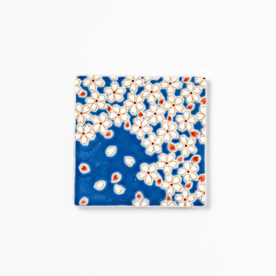Square blue Japanese ceramic coaster with white sakura blossom and petal design for traditional dining.