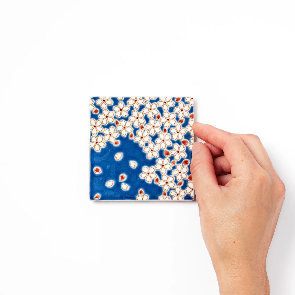 Square blue Japanese ceramic coaster with white sakura blossom and petal design for traditional dining.