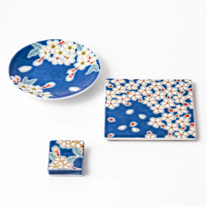 Japanese ceramic tableware set with blue dishes and chopstick rest decorated with white sakura blossoms.