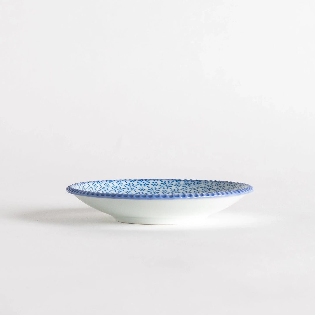 A round ceramic plate with a delicate blue floral pattern, bordered by a textured rim.