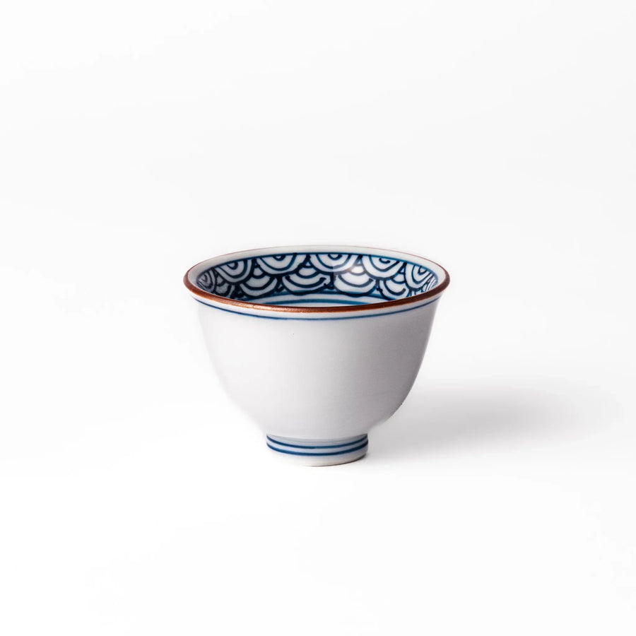 Porcelain sake cup with a white exterior and interior featuring traditional blue wave patterns and a warm brownish rim.