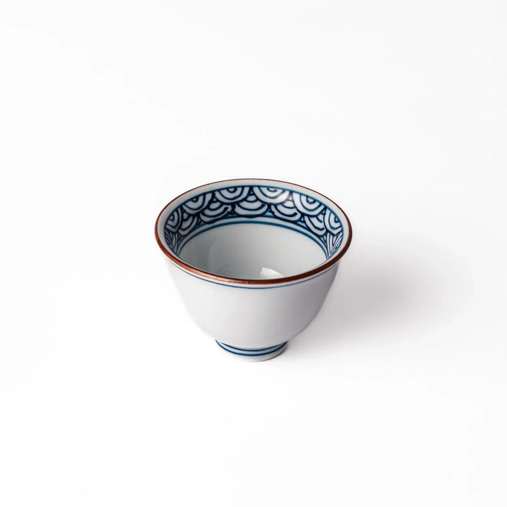 Porcelain sake cup with a white exterior and interior featuring traditional blue wave patterns and a warm brownish rim.