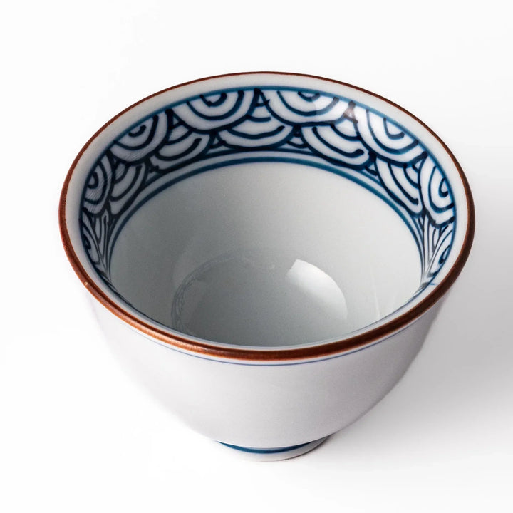Porcelain sake cup with a white exterior and interior featuring traditional blue wave patterns and a warm brownish rim.
