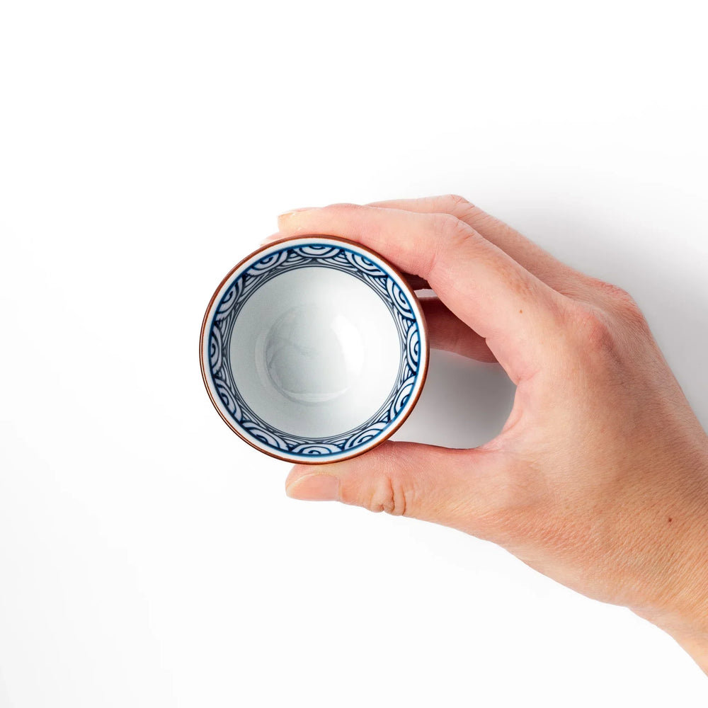 Porcelain sake cup with a white exterior and interior featuring traditional blue wave patterns and a warm brownish rim.