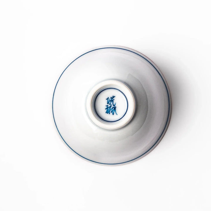 Porcelain sake cup with a white exterior and interior featuring traditional blue wave patterns and a warm brownish rim.