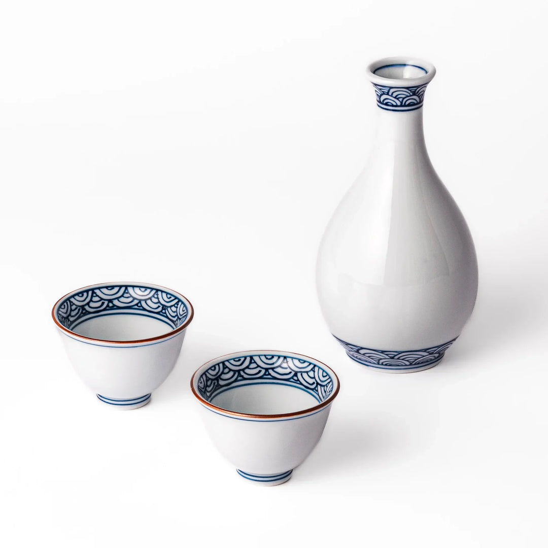 Three piece Japanese porcelain sake set with white flask and cups featuring blue wave and red brown rims.