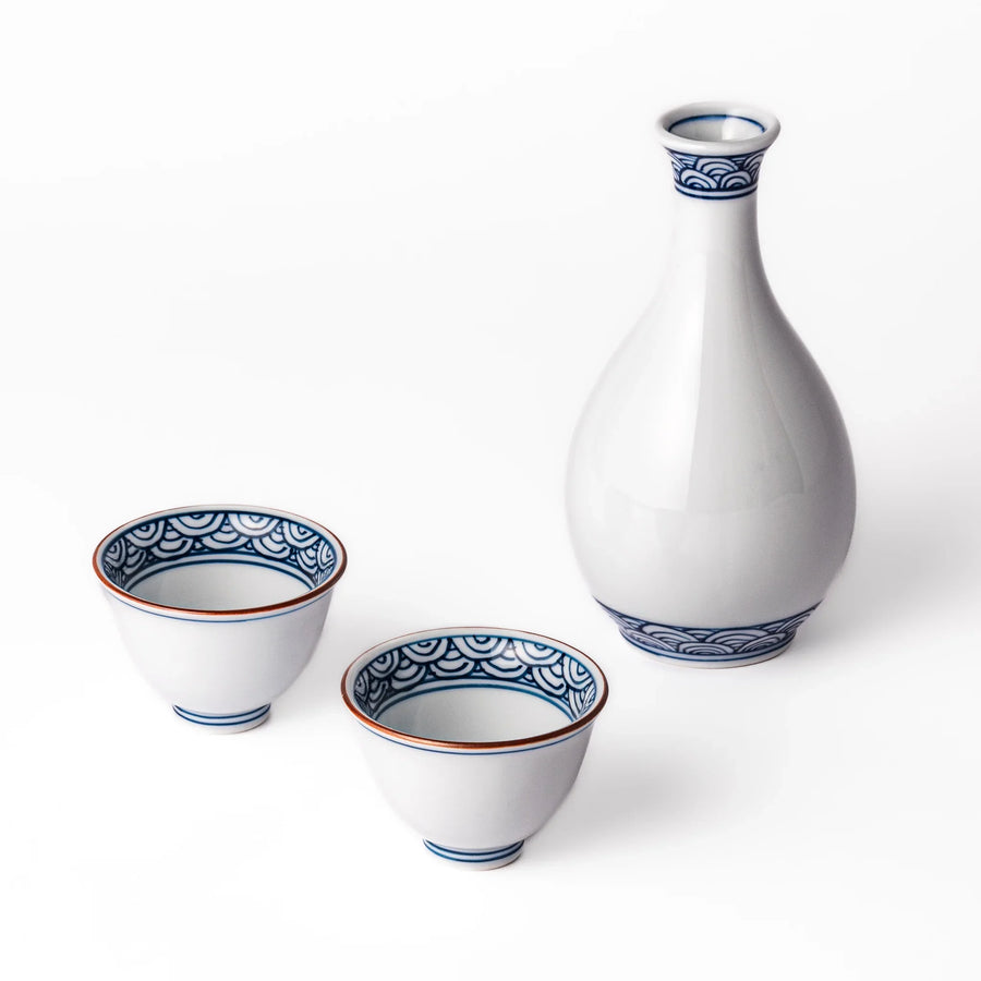 Three piece Japanese porcelain sake set with white flask and cups featuring blue wave and red brown rims.