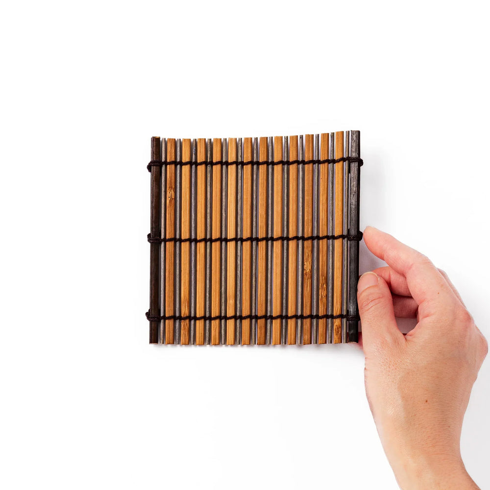 Brown bamboo coaster with alternating dark and natural slats bound with black cord for rustic table style.