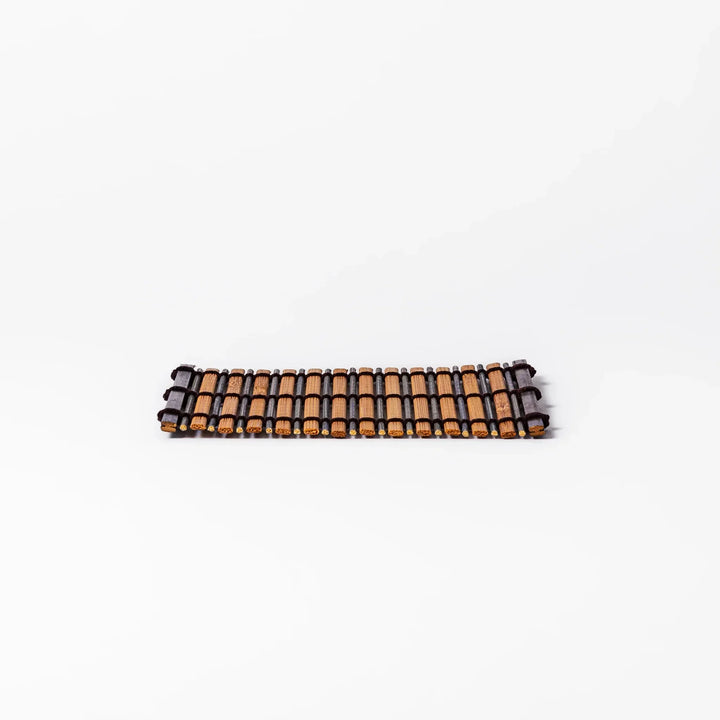 Brown bamboo coaster with alternating dark and natural slats bound with black cord for rustic table style.