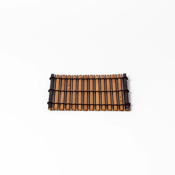 Brown bamboo coaster with alternating dark and natural slats bound with black cord for rustic table style.