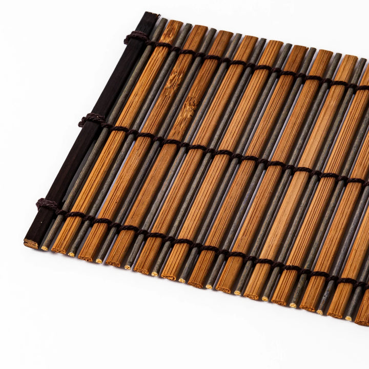 Brown bamboo coaster with alternating dark and natural slats bound with black cord for rustic table style.