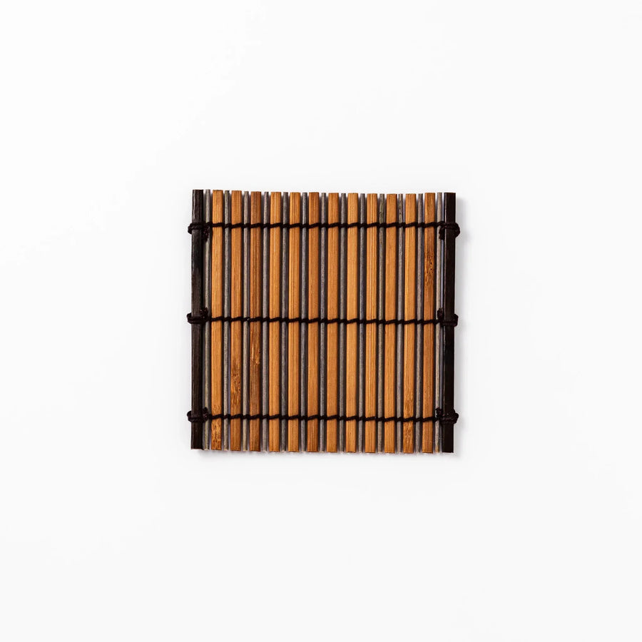 Brown bamboo coaster with alternating dark and natural slats bound with black cord for rustic table style.