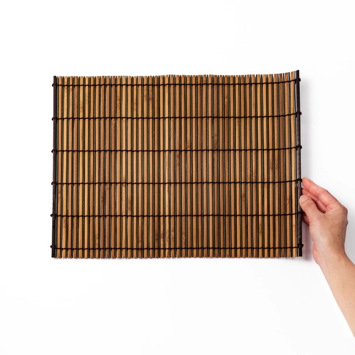Brown bamboo table mat with dark and natural slats bound with black cord for warm Japanese table settings.