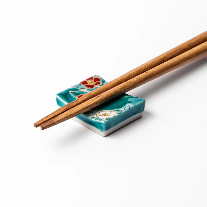 Japanese ceramic chopstick rest with red and white camellia blossoms on glossy teal background for elegance.