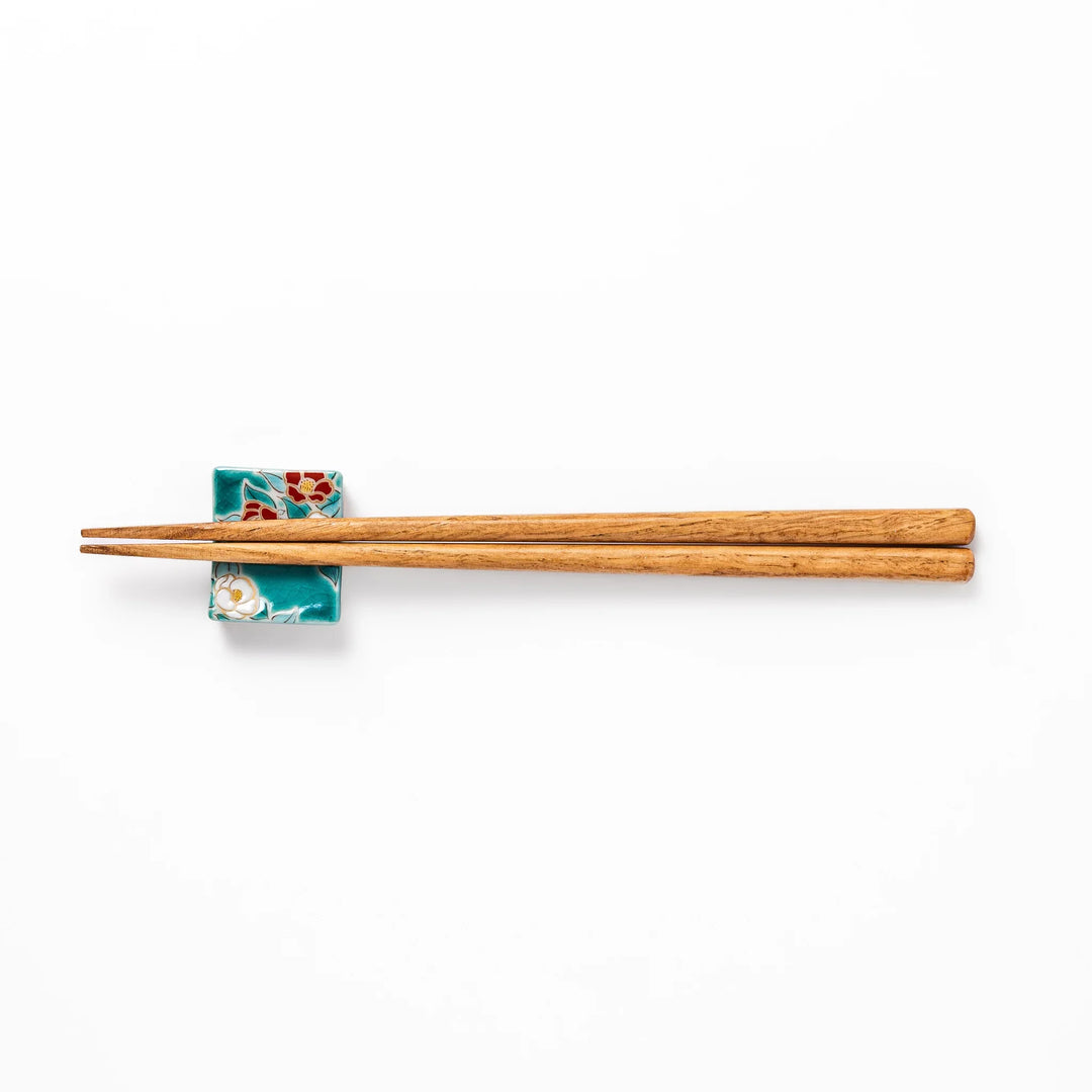 Japanese ceramic chopstick rest with red and white camellia blossoms on glossy teal background for elegance.