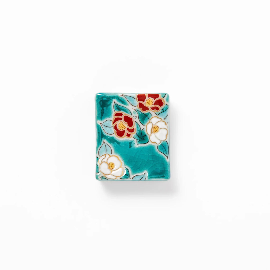 Japanese ceramic chopstick rest with red and white camellia blossoms on glossy teal background for elegance.