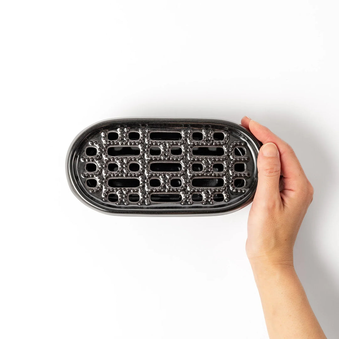 Black Japanese ceramic daikon oroshi grater with built in dish and wide holes for smooth grating cleanup.